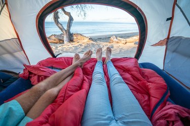 Point of view of couple's feet from inside a tent camping on the beach