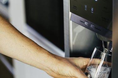 Pouring cold water and ice cubes from dispenser of home fridge