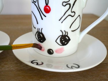 A paintbrush applying red blush cheeks to a mug