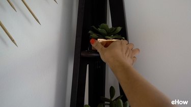 Placing a faux succulent on a corner shelf.