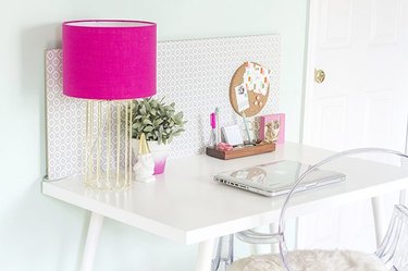 Modern desk with a pink lamp and a clear chair