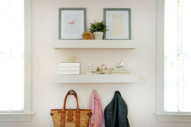 Two white floating shelves over hangers and holding photos and a plant