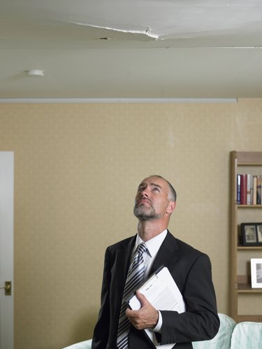 Mature man in suit with clipboard looking up at crack in ceiling