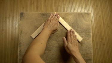 Gluing wood stir sticks to tabletop in herringbone pattern.