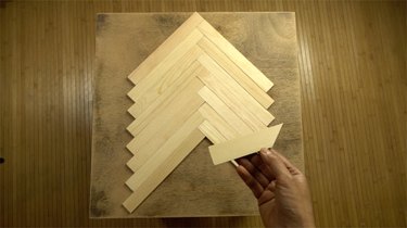Measuring and cutting paint stir sticks to tabletop to create herringbone pattern.