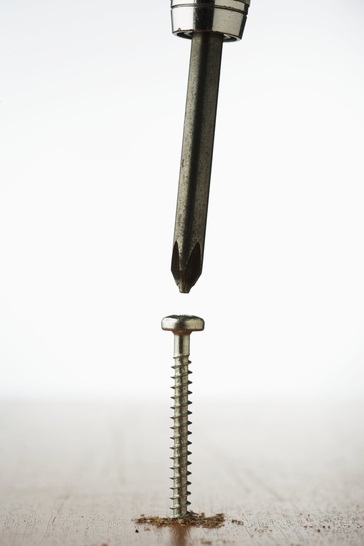 Crosshead screwdriver above screw sticking out of wood, close-up