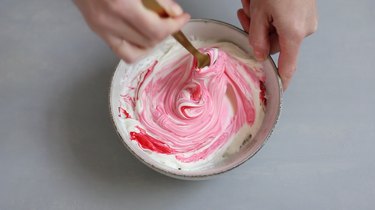 Mixing pink food coloring into frosting