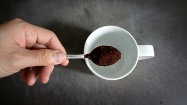Hand Holding Spoon Of Coffee Powder Over Cup