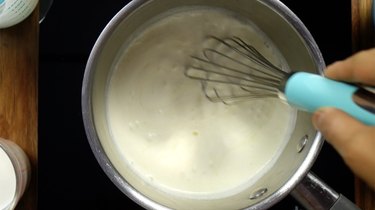 Mixing sugar-free sweetener into heavy cream in saucepan for sugar-free Irish cream liqueur.