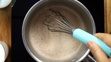 Mixing cocoa into heavy cream in saucepan for sugar-free Irish cream liqueur.