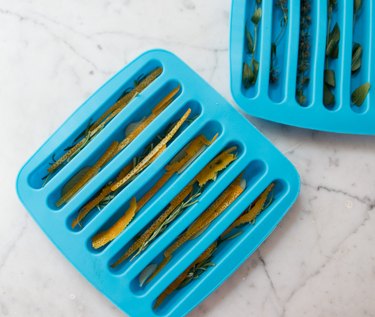 Ice cube molds packed with fresh herbs and citrus peels
