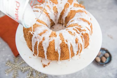 Bundt cake on a cake stand with glaze being poured over it