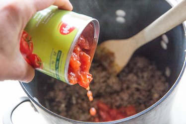 pouring diced tomatoes into a pot