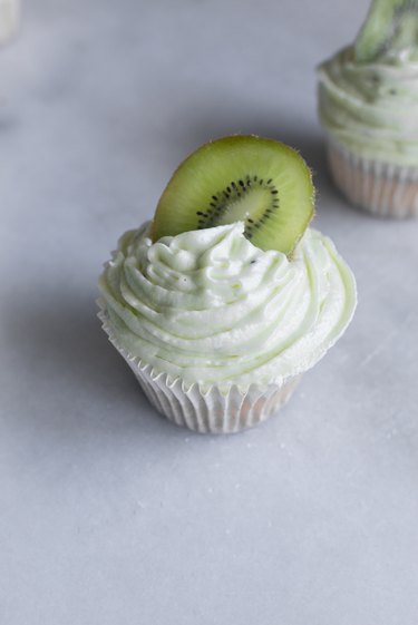 Generously frost the cupcakes and top with a kiwi slice.