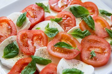 tomatoes and mozzarella on a platter with salt, pepper, and basil