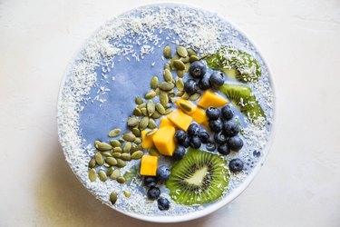 blue smoothie bowl with fresh fruit, shredded coconut and pumpkin seeds