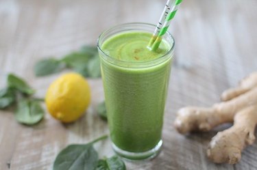 A glass of a green detoxifying smoothie next to spinach leaves, ginger and a lemon.