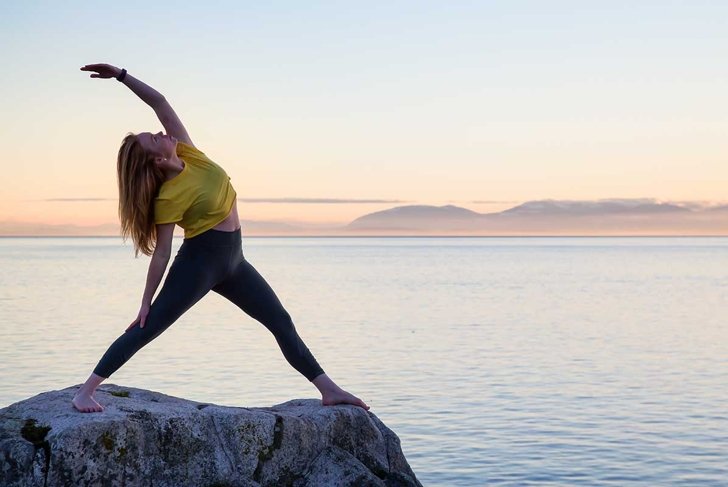 Young woman practicing yoga on a rocky island during a vibrant sunset. Taken in Whytecliff Park, Horseshoe Bay, West Vancouver, British Columbia, Canada.