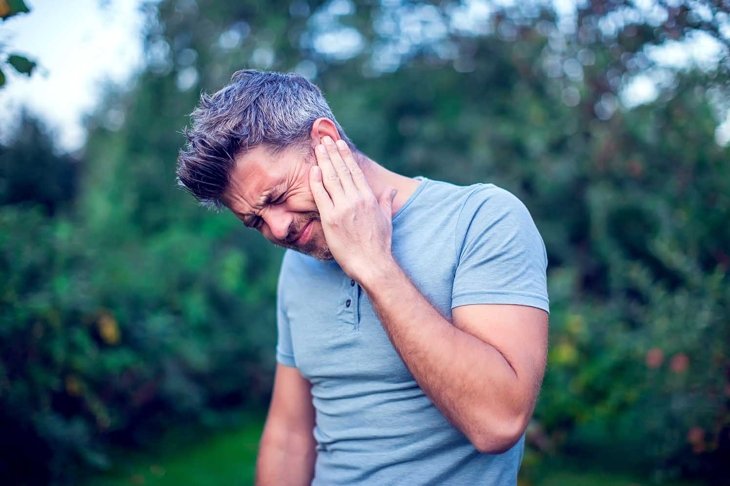 Unhappy man having ear pain touching his painful head outdoor
