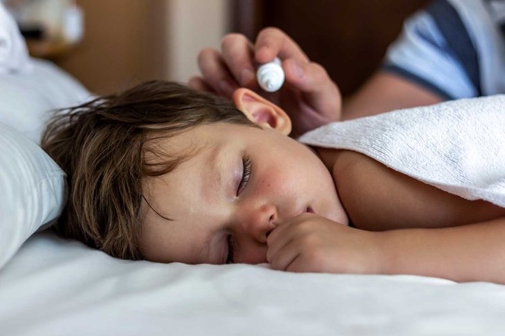 Man buries drops in a boy's ear. Treatment of ear diseases. Medical pipette with a drop of medication over the patient's ear. Young father using ear drops to his sleeping son at home. Copy space.